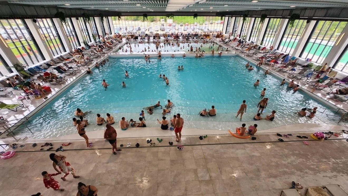 Посетители крытого термального бассейна — десятки людей купаются и отдыхают у воды