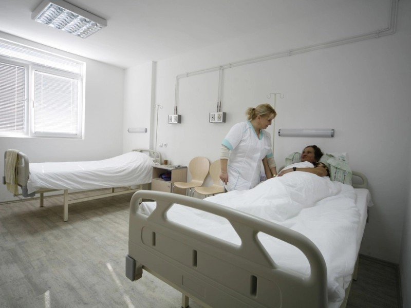 Палата хирургического отделения УМБАЛ «Каспела»: медсестра у постели пациентки в светлом помещении с современным оснащением