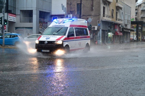 Карета скорой помощи едет по затопленной дождём улице во время шторма в Греции