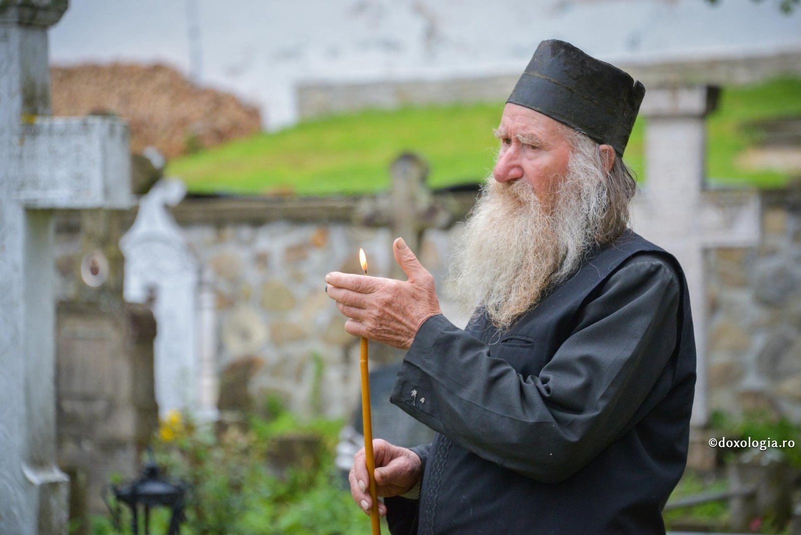 Православный священник со свечой на сельском кладбище во время поминовения