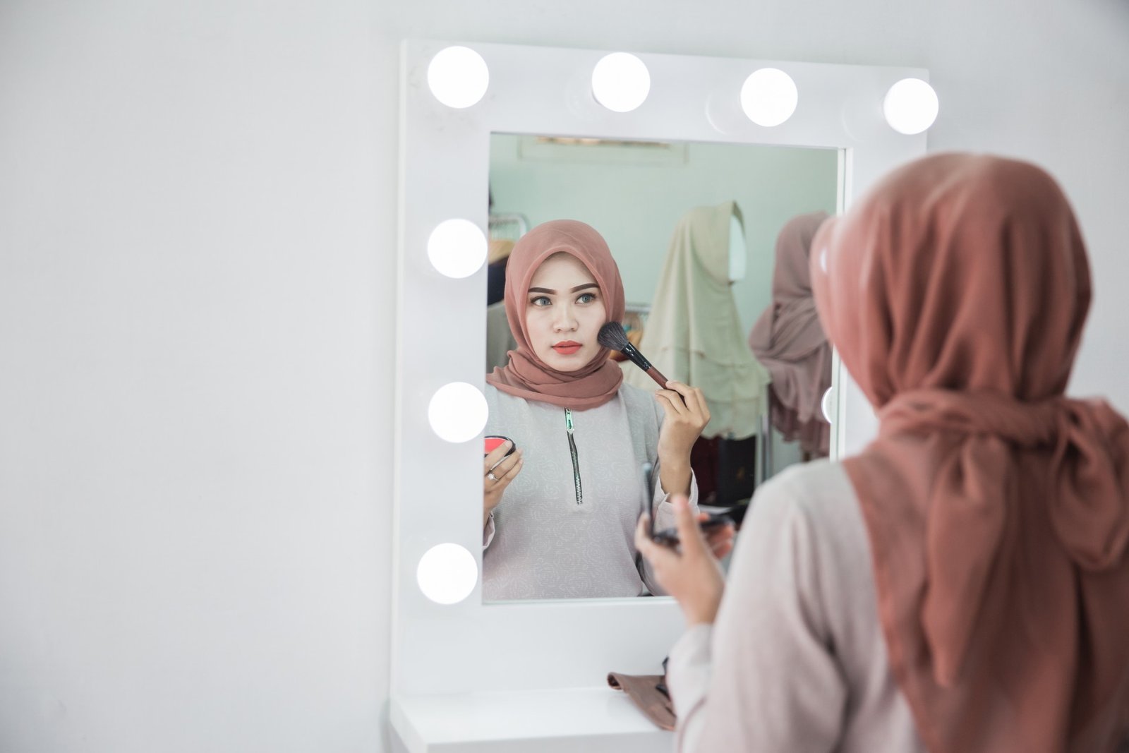 Клиентка наносит макияж перед зеркалом с лампами в салоне красоты — именно салоны и их поставщики с 1 мая будут работать по обновлённому регламенту