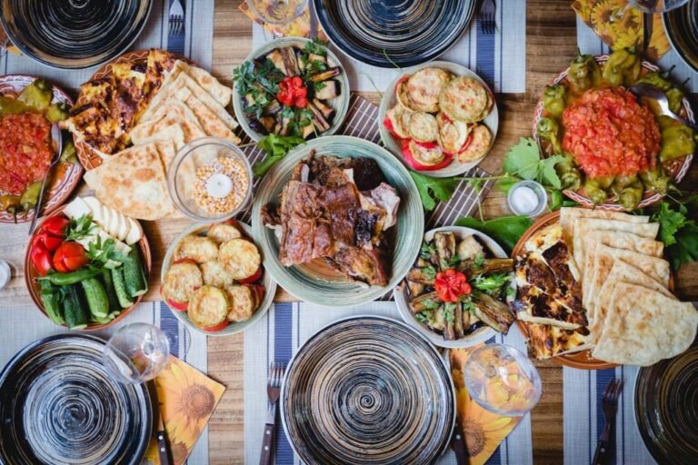 Стол, сервированный блюдами традиционной молдавской сельской кухни: плэчинты, овощные закуски, жаркое, домашний хлеб и соусы в глиняной посуде