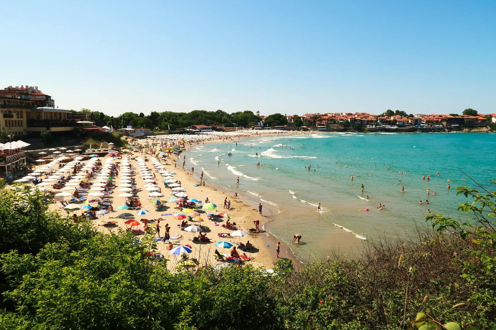 Пляж Созополя с рядами зонтиков и отдыхающими у бирюзовой воды Чёрного моря