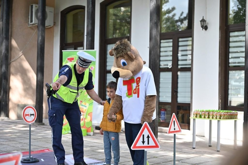 Сотрудник дорожной полиции показывает мальчику оборудование для контроля скорости рядом с талисманом кампании TEDI у входа в детский сад в Пловдиве