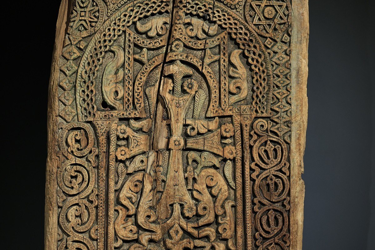 Крупный план резной деревянной панели с центральной фигурой и крестом, окружённой сложными орнаментальными узорами и зооморфными мотивами