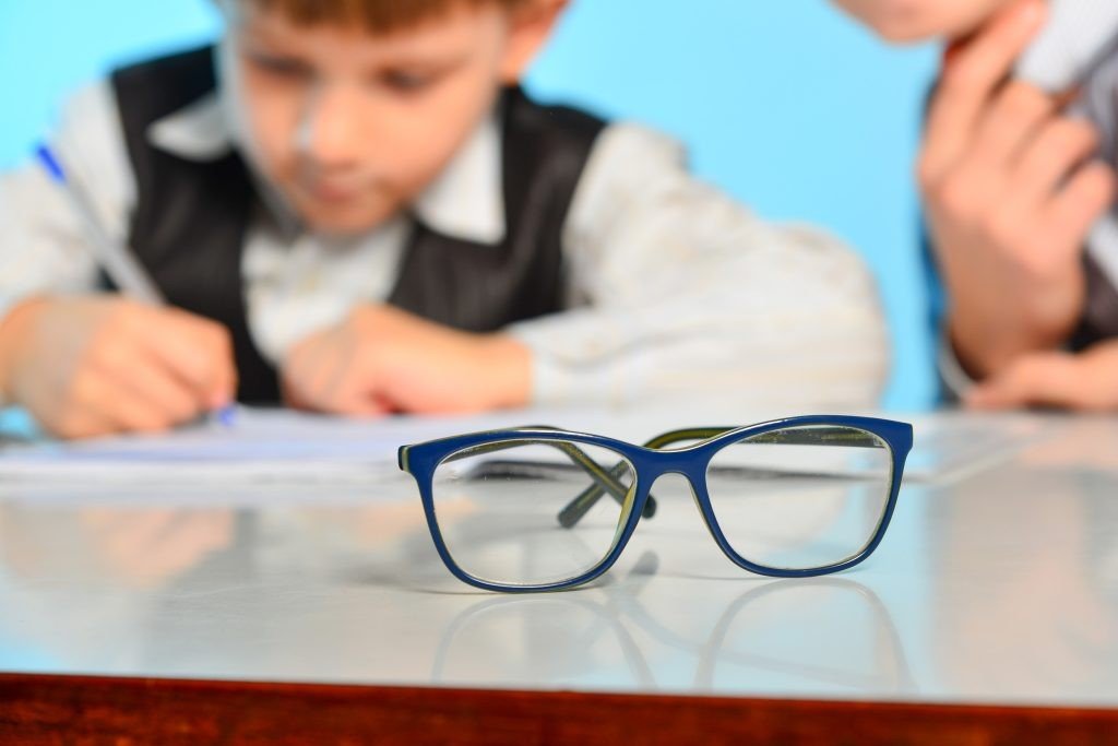 Детские очки на парте, ребёнок пишет на заднем плане — проблема зрения у школьников в Греции