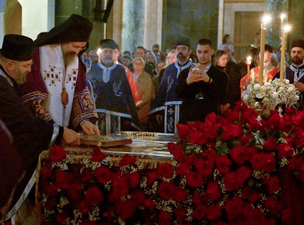 Священнослужители проводят обряд у алтаря, украшенного красными розами, в окружении верующих со свечами