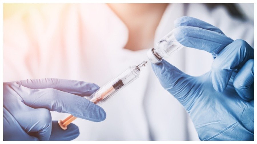 Руки в синих перчатках набирают вакцину из ампулы в шприц