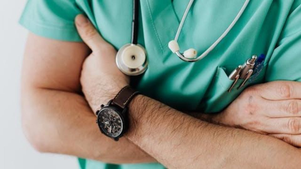 Врач в зелёной униформе со стетоскопом на шее и скрещёнными руками — собирательный образ дефицитной профессии семейного врача в Румынии