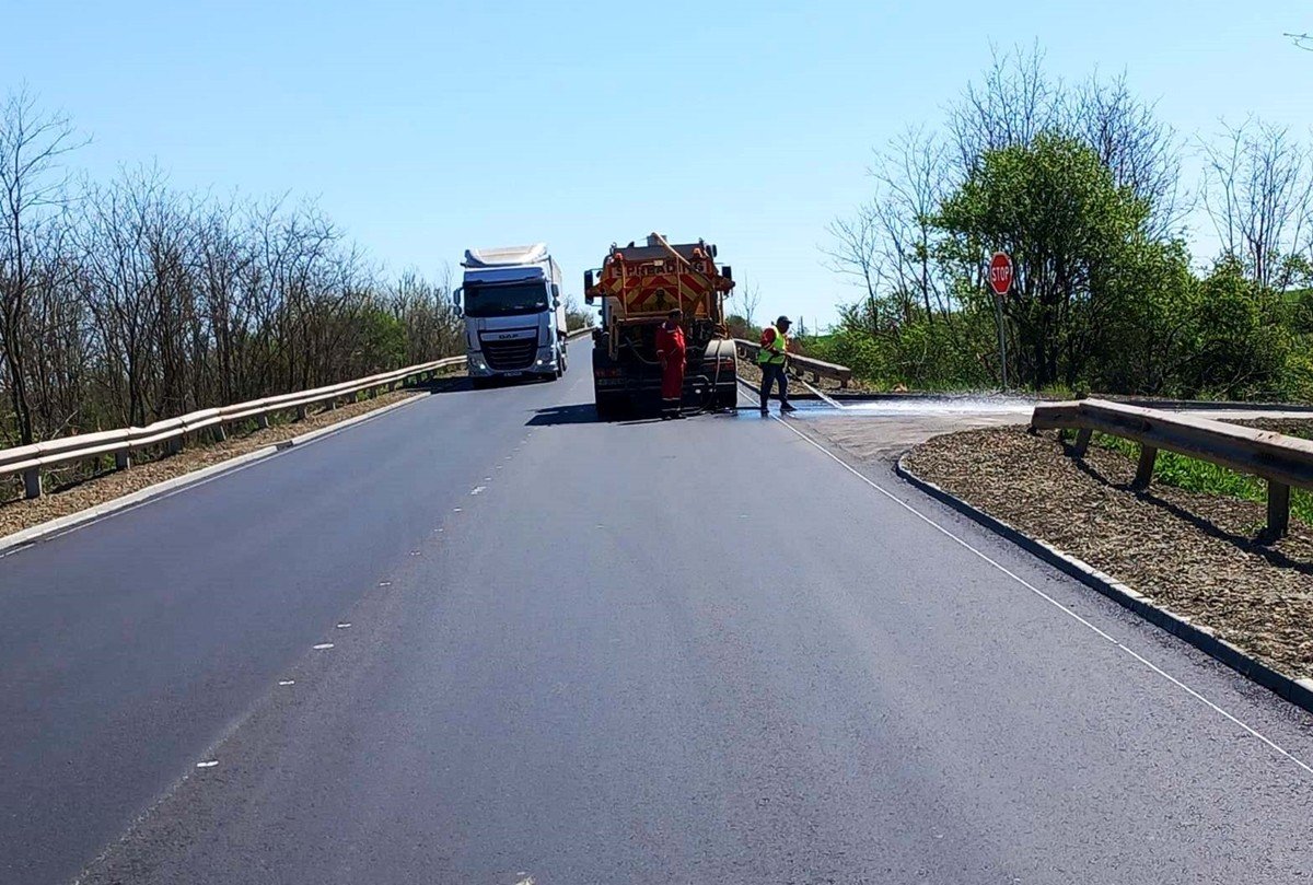 Дорожные рабочие наносят разметку на трассе, на заднем плане ждёт грузовик