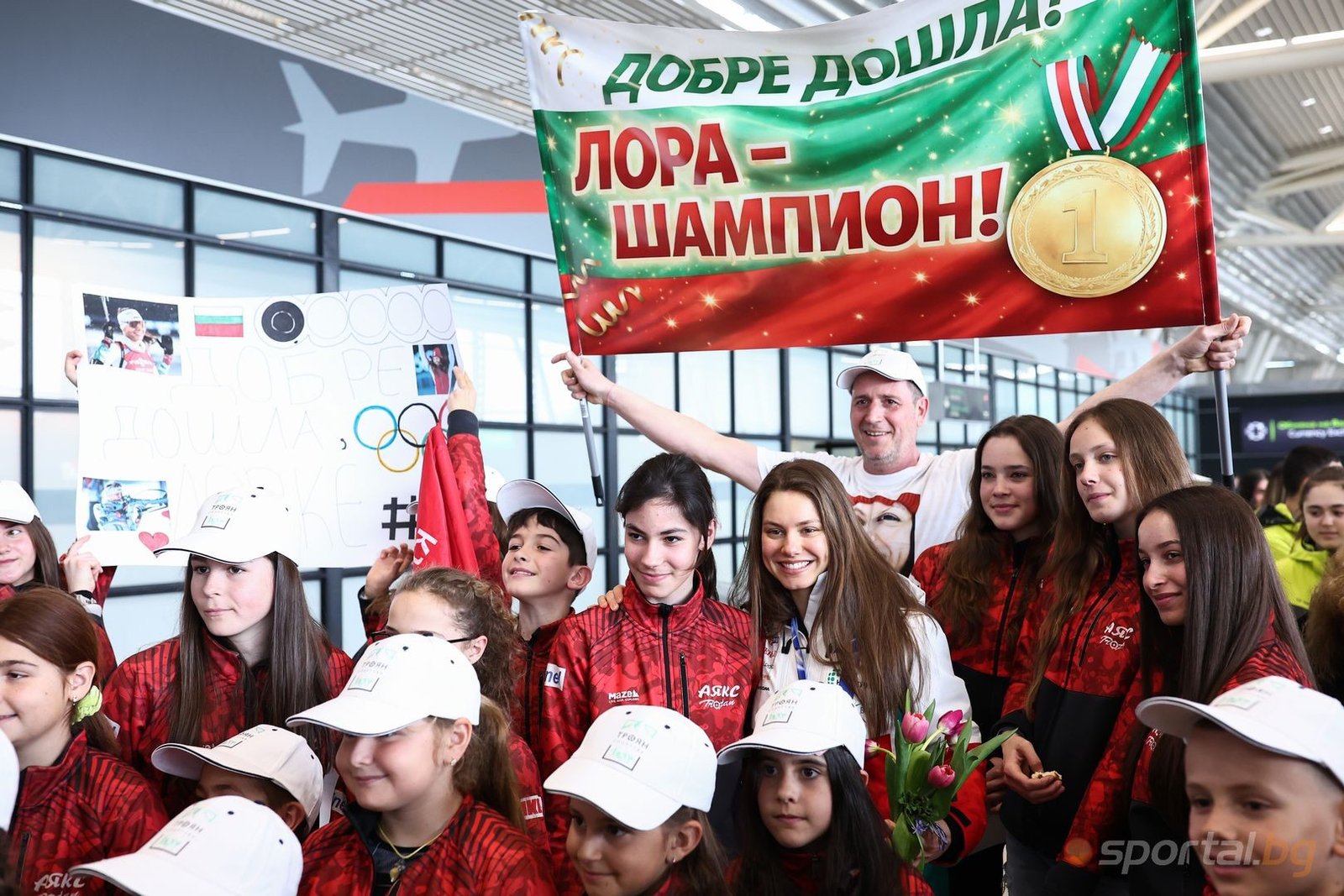 Лора Христова среди юных болельщиков с приветственным плакатом в аэропорту