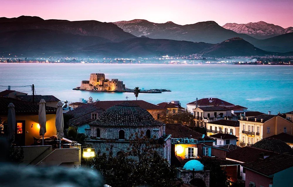 Нафплион в сумерках — старый город с черепичными крышами и крепость Бурдзи посреди залива на фоне подсвеченных гор