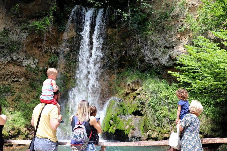 Семьи смотрят на каскадный водопад Лисине, поросший мхом каменный уступ, в окружении зелёных деревьев