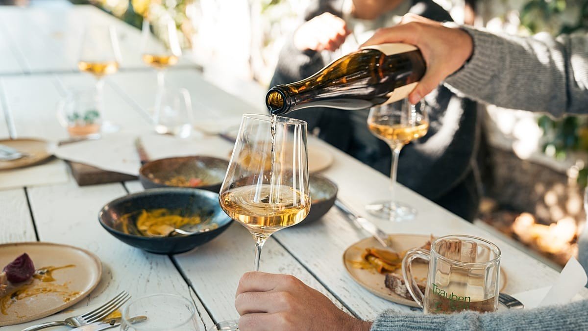 Золотистое белое вино наливают в бокал за столом с закусками