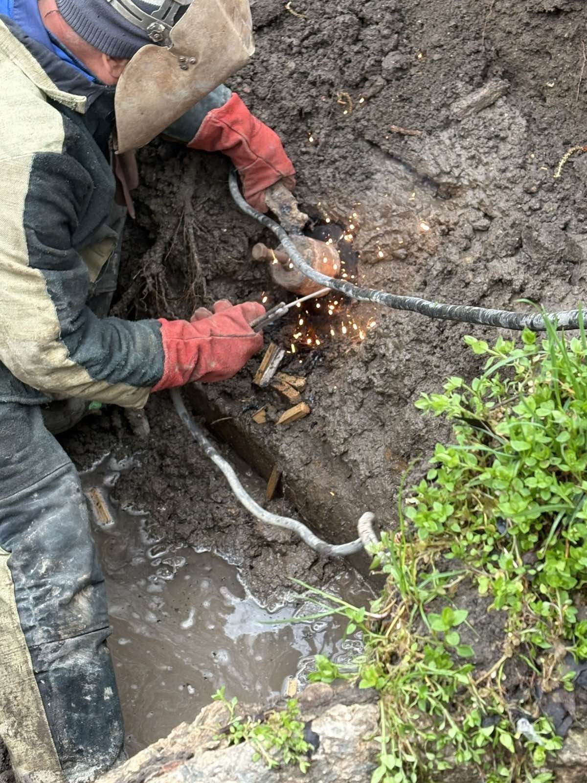 Крупный план: сварщик S.A. „Apă-Canal Chișinău” соединяет участки металлической водопроводной трубы в траншее с грунтовой водой, искры разлетаются от шва