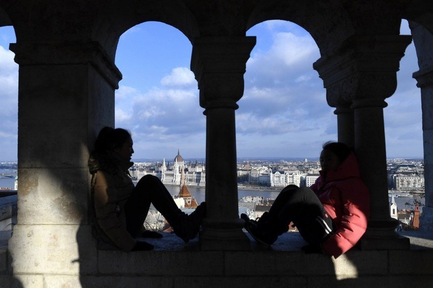 Две туристки сидят в аркадах Рыбацкого бастиона в Будапеште с видом на здание Парламента за Дунаем