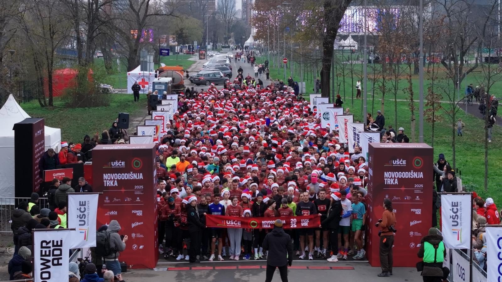 Старт Новогодней гонки 2025 на Ушче: участники в шапках Санта-Клауса готовятся к забегу между воротами NOVOGODIŠNJA TRKA