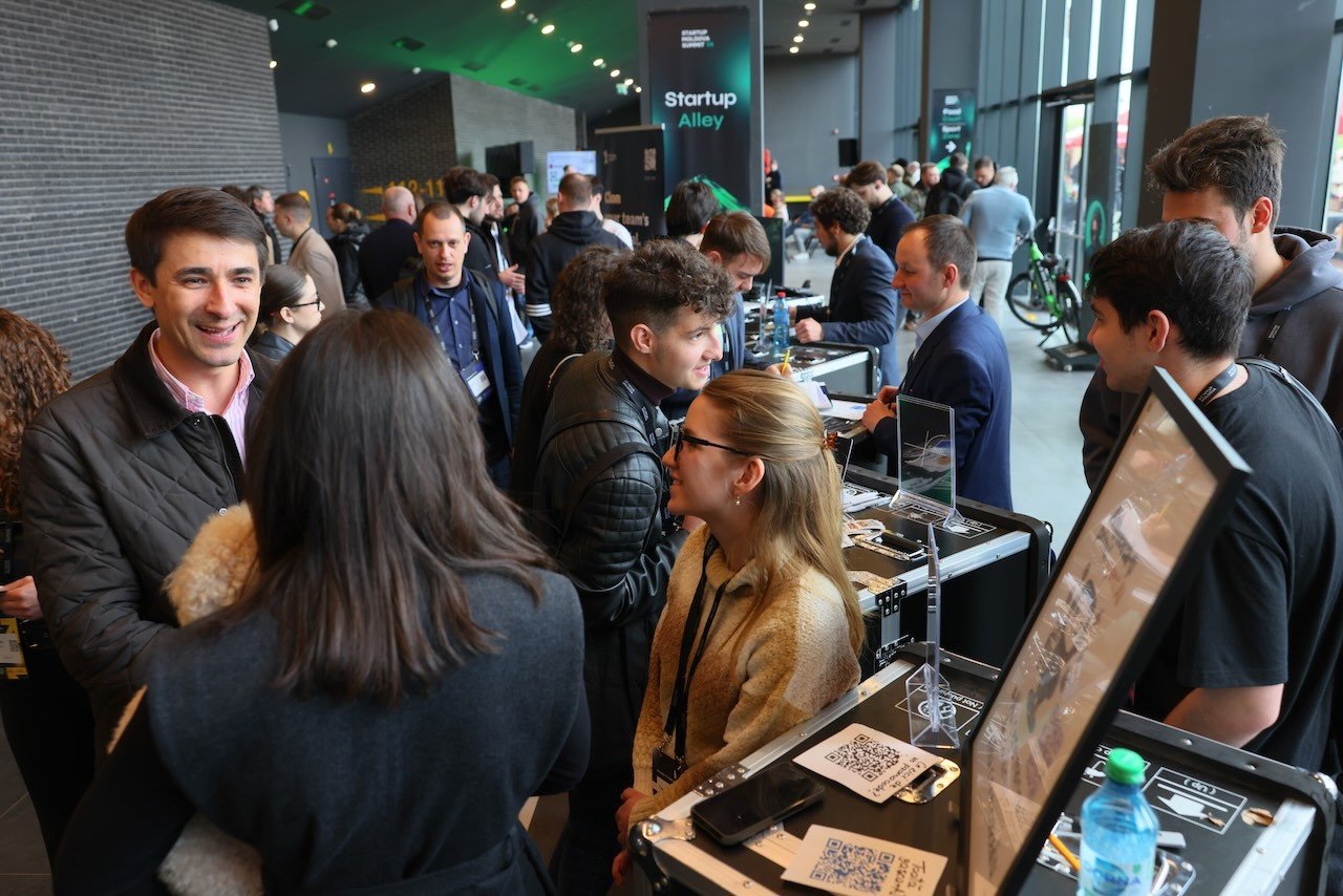 Зона Startup Alley на Startup Moldova Summit 2026: основатели демонстрируют прототипы и демо-стенды со сканируемыми QR-кодами, пока посетители тестируют устройства и знакомятся с командами молдавских стартапов
