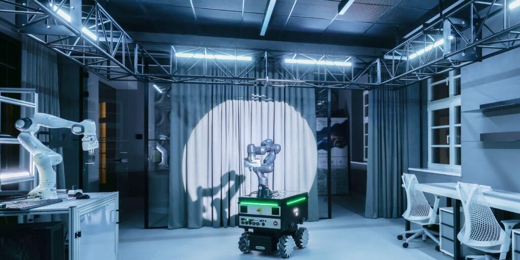 Лаборатория робототехники в Палате науки: промышленный манипулятор слева и мобильный робот в круге прожектора — демонстрационная зона автоматизации