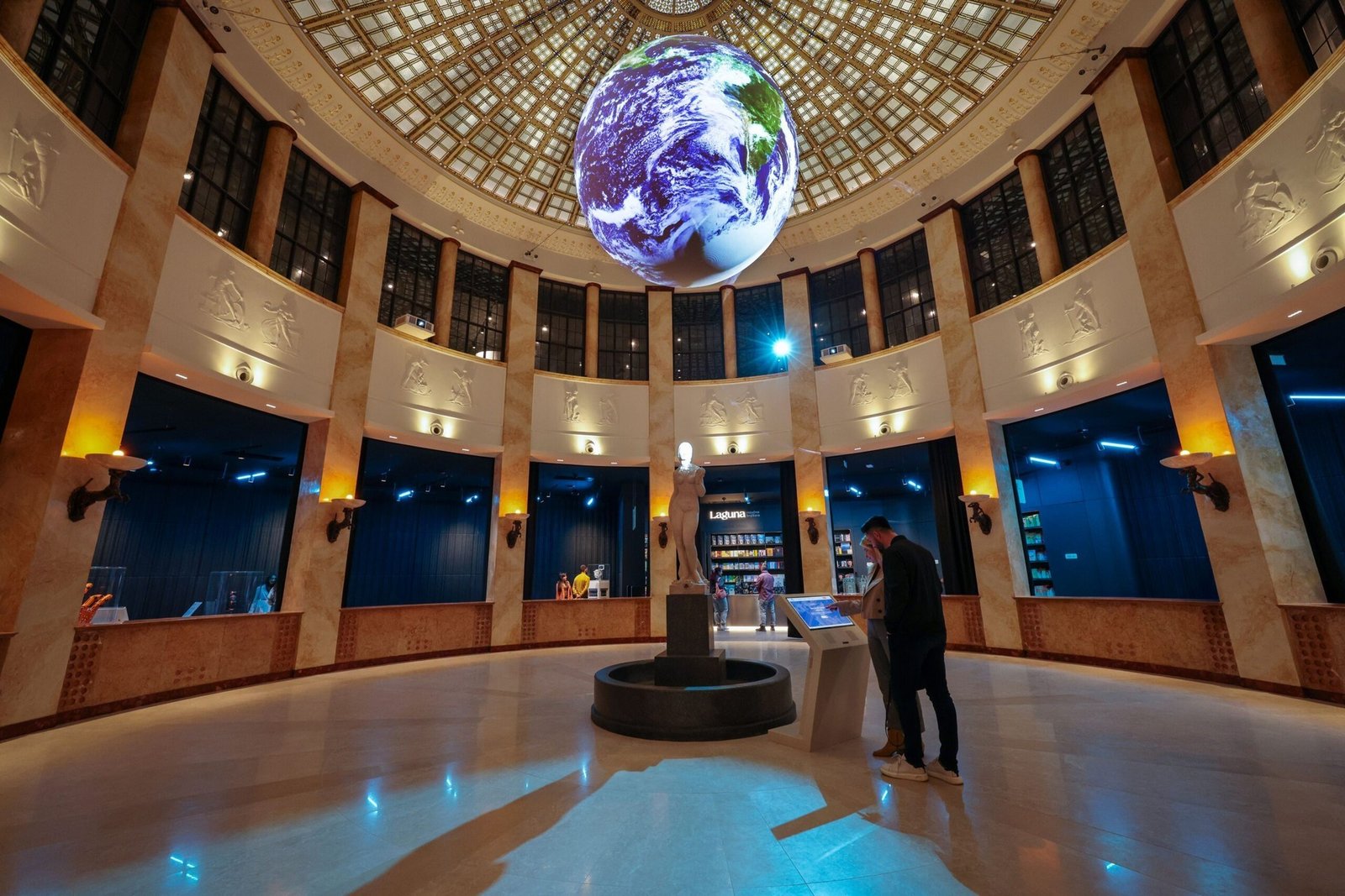 Внутренняя ротонда Палаты науки с гигантским светодиодным глобусом Земли под стеклянным куполом; посетители у интерактивного киоска возле скульптурного фонтана