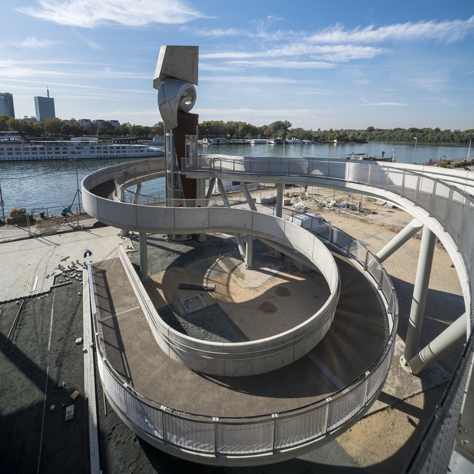 Спиральный пешеходный мост из бетона и металла с вертикальной скульптурой на берегу Дуная