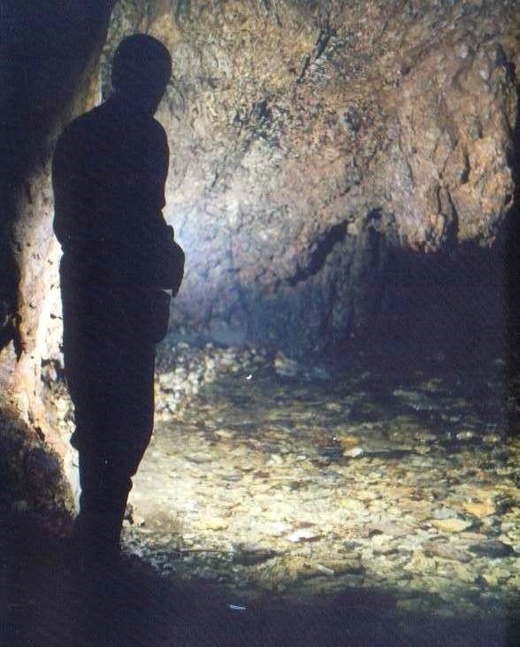 Силуэт исследователя на фоне освещённого зала карстовой пещеры в уезде Горж: пол усыпан гравием, отполированным подземным ручьём