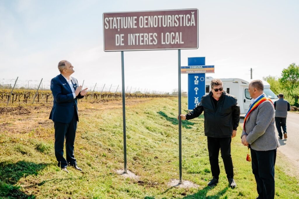 Представители властей у дорожной таблички первой оенотуристической стации Румынии в Гура-Вадулуй на фоне виноградников