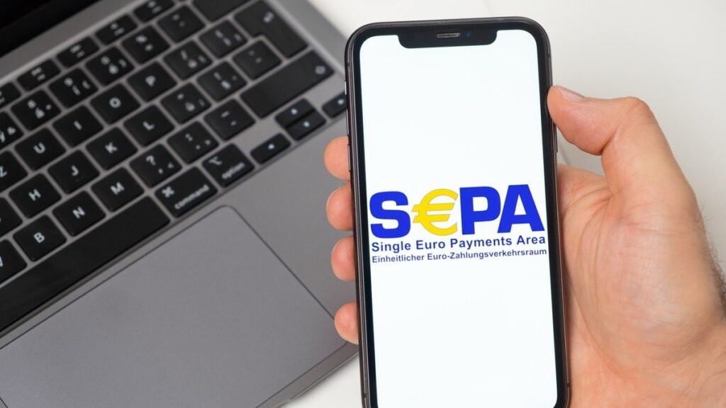 Смартфон с логотипом Single Euro Payments Area на экране на фоне ноутбука — иллюстрация присоединения Сербии к SEPA