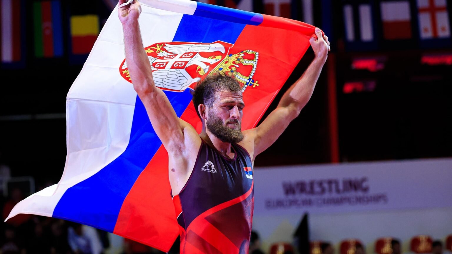 Георгий Тибилов поднимает над головой сербский флаг после победы в финале Чемпионата Европы по греко-римской борьбе в весовой категории до 60 кг, Тирана, 22 апреля 2026 года