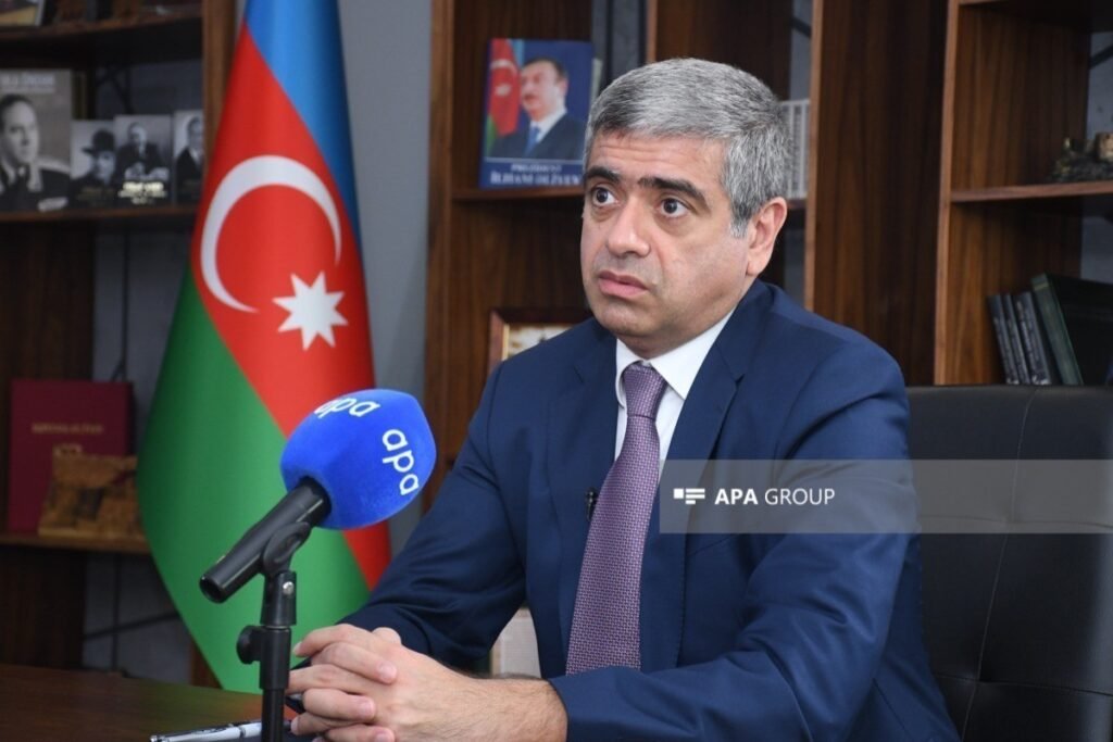 Руководитель центрального аппарата Министерства здравоохранения Азербайджана Анар Алиев даёт интервью в кабинете на фоне государственного флага — поясняет цели объединения агентств в сфере здравоохранения