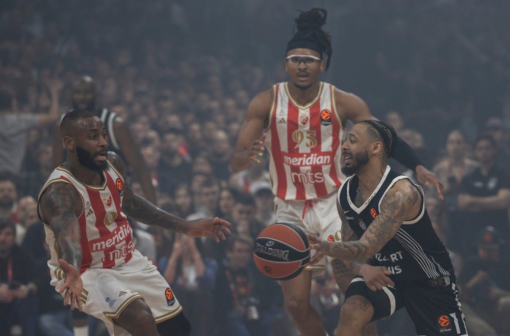 Игрок Партизана отдаёт передачу в борьбе с двумя баскетболистами Црвены Звезды на фоне задымлённых трибун белградского дерби Евролиги