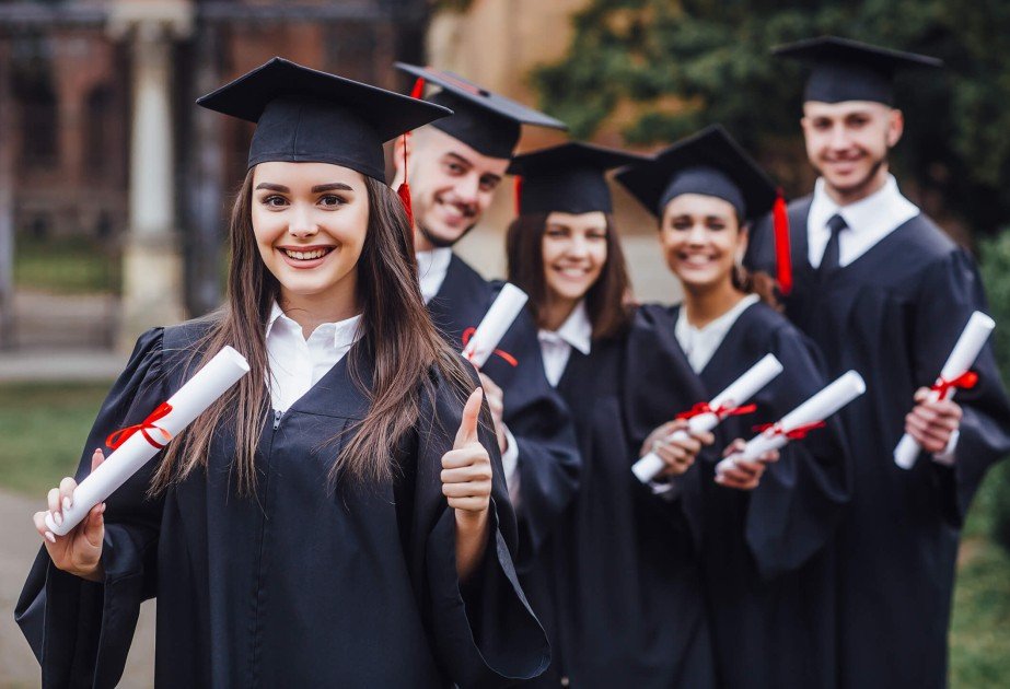 Выпускники университета в мантиях и академических шапочках с дипломами в руках празднуют окончание учёбы