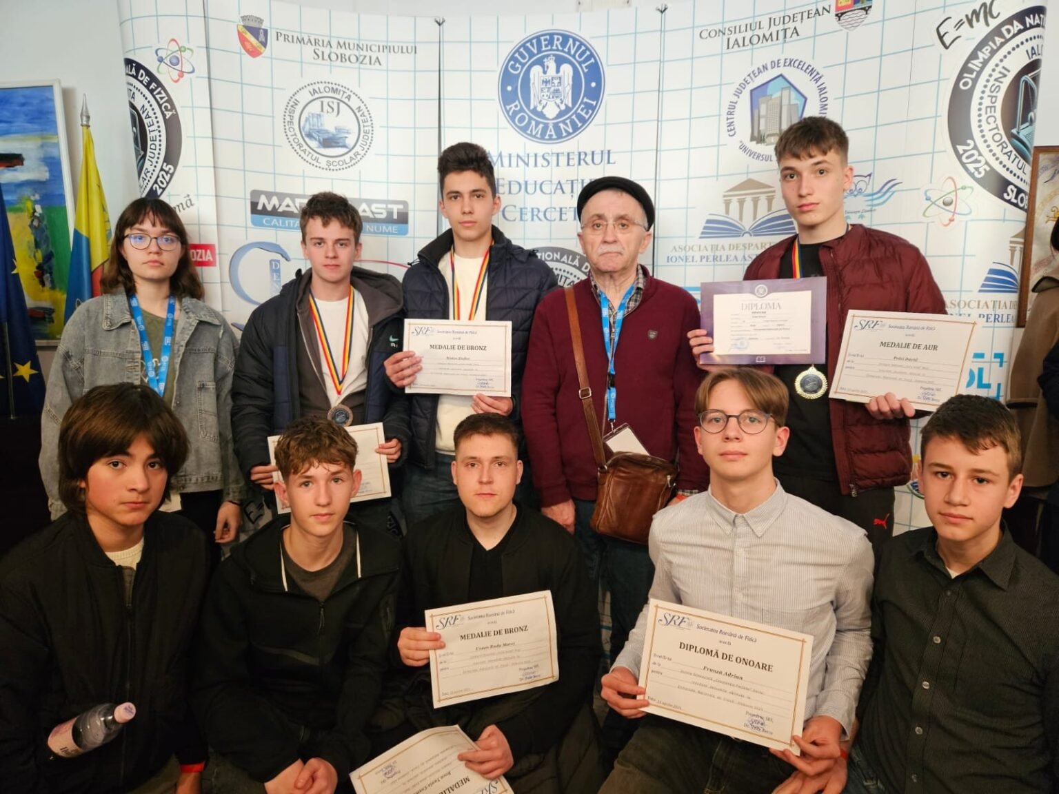 Ученики из уезда Васлуй с медалями и дипломами на церемонии награждения Национальной олимпиады по физике на фоне баннера Министерства образования Румынии