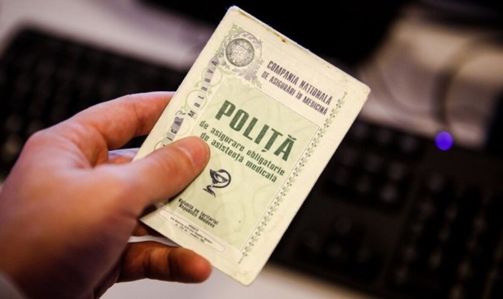 Рука держит полис обязательного медицинского страхования Молдовы на фоне клавиатуры