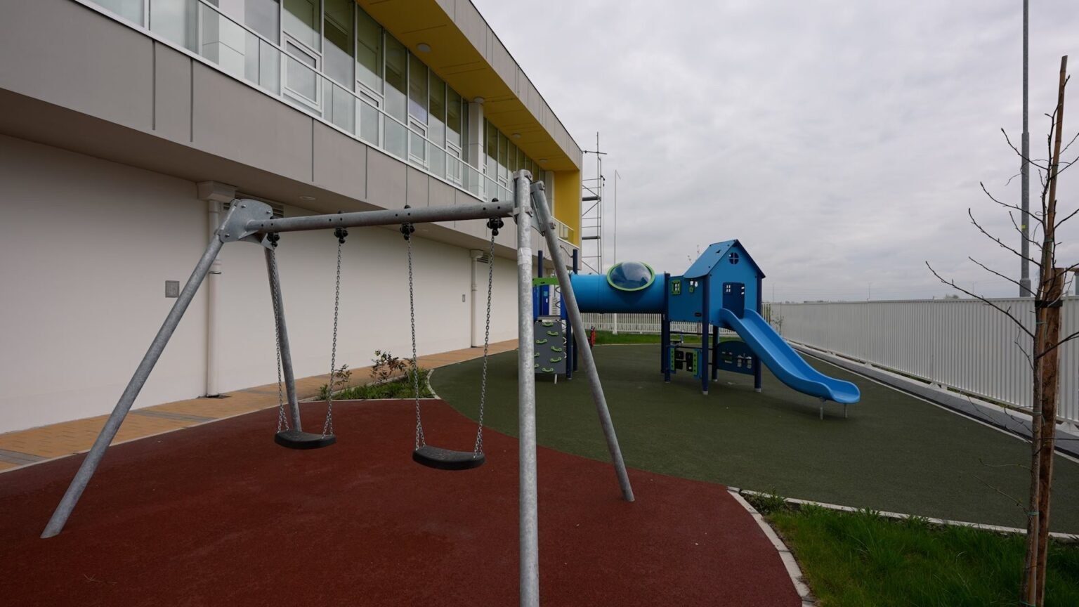 Детская площадка с качелями и синей горкой на территории детского сада в Белграде