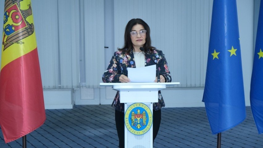 Представительница Министерства образования за трибуной с государственным гербом Молдовы; по сторонам — флаги Молдовы и Евросоюза