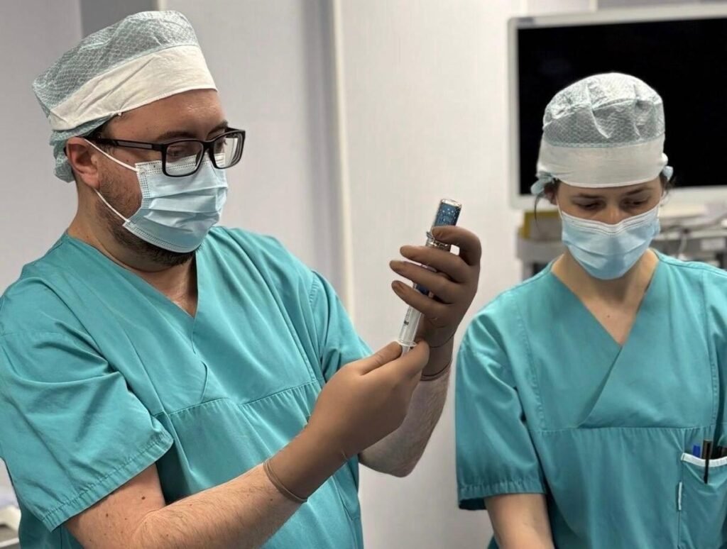 Врачи в хирургических костюмах и масках готовят препарат в операционной