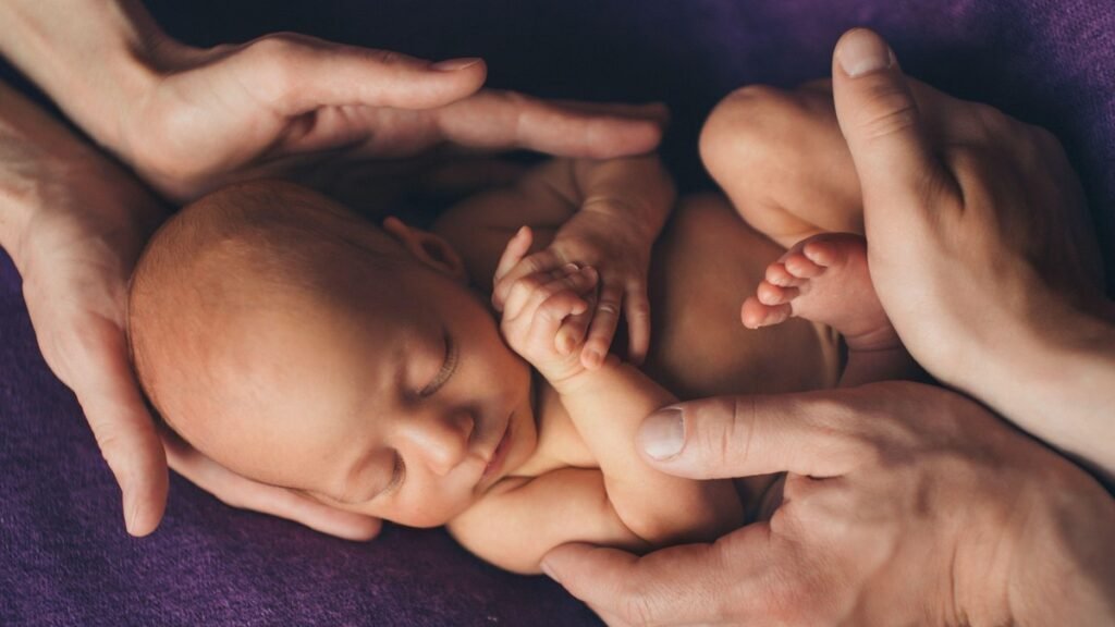 Новорождённый ребёнок спит на фиолетовой ткани в бережных ладонях родителей — образ родительства благодаря вспомогательным репродуктивным технологиям