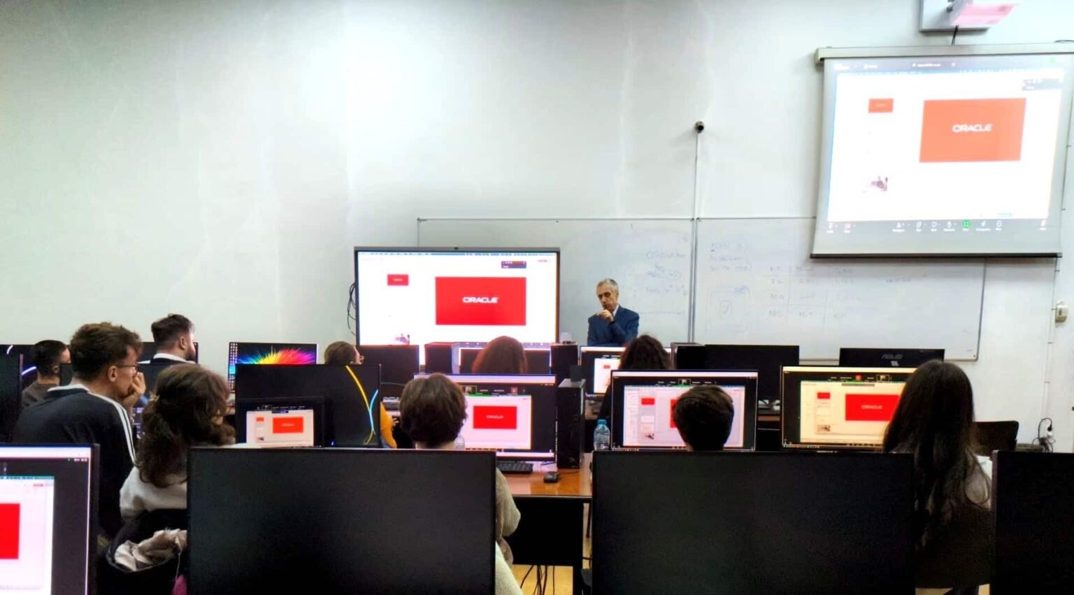 Участники воркшопа Oracle Academy в румынском университете работают за компьютерами, пока преподаватель демонстрирует слайды по настройке производительности баз данных