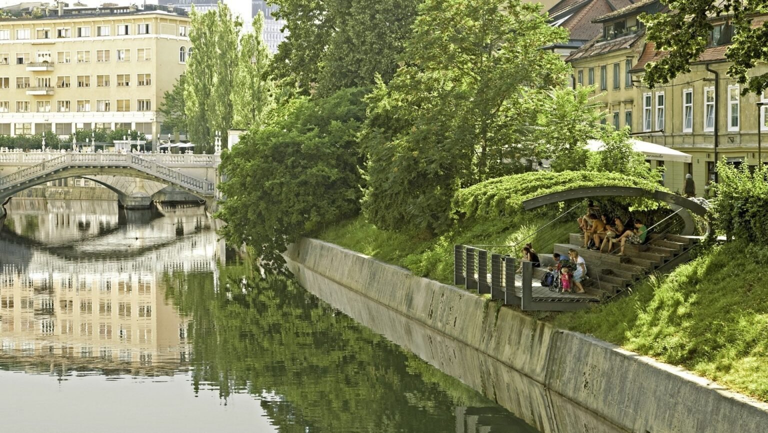 Деревянный павильон на берегу Любляницы среди зелёных деревьев и каменной набережной