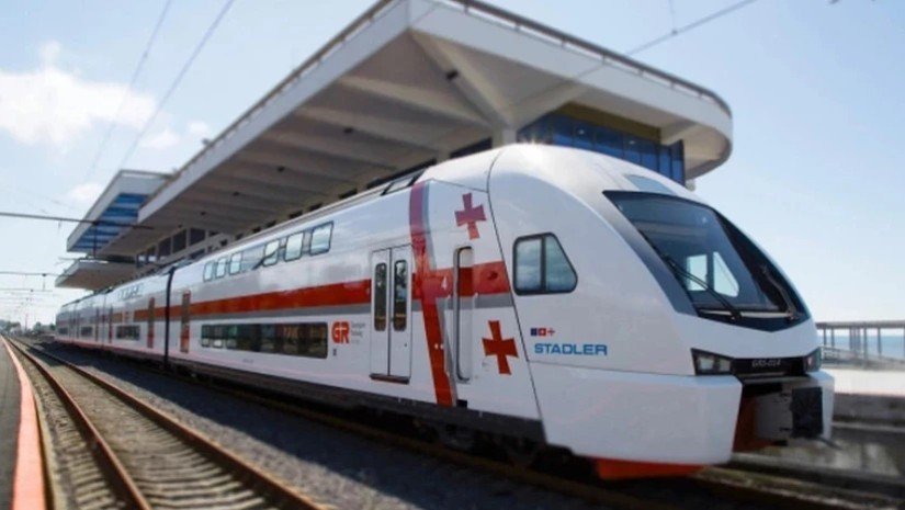 Грузия перезапускает «Кукушку» и ускоряет путь к морю Современный двухэтажный поезд Stadler с символикой грузинского флага на железнодорожной платформе