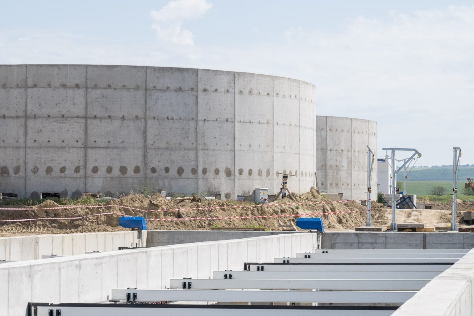Большие бетонные резервуары строящейся станции очистки сточных вод в Кагуле с металлическими конструкциями и земляными работами на переднем плане