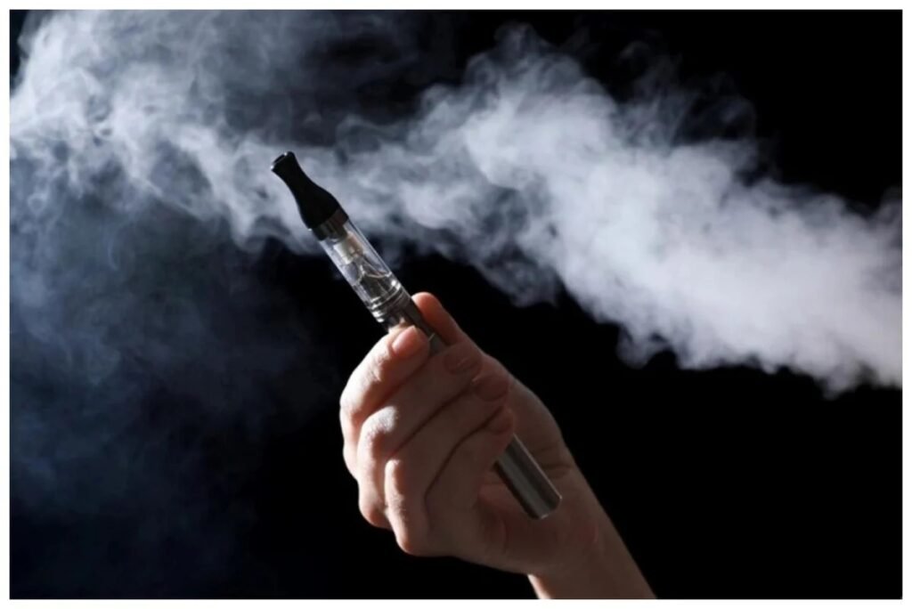 Рука держит электронную сигарету, из которой поднимается густое облако пара на тёмном фоне