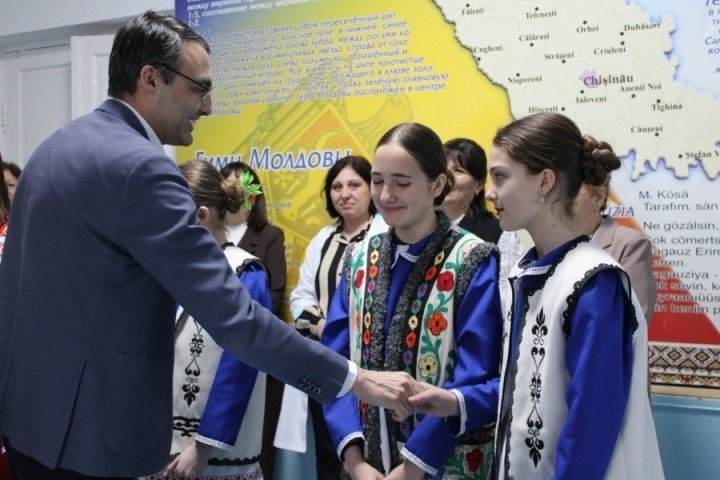 Представитель Министерства образования приветствует учениц в национальных костюмах на фоне карты Молдовы в модельном кабинете румынского языка