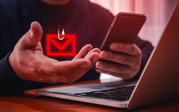 Человек держит смартфон рядом с ноутбуком, на экране &mdash; значок фишингового письма, иллюстрирующий схему онлайн-мошенничества