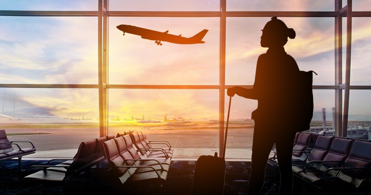 Силуэт путешественницы в зале ожидания аэропорта на фоне взлетающего самолёта на закате