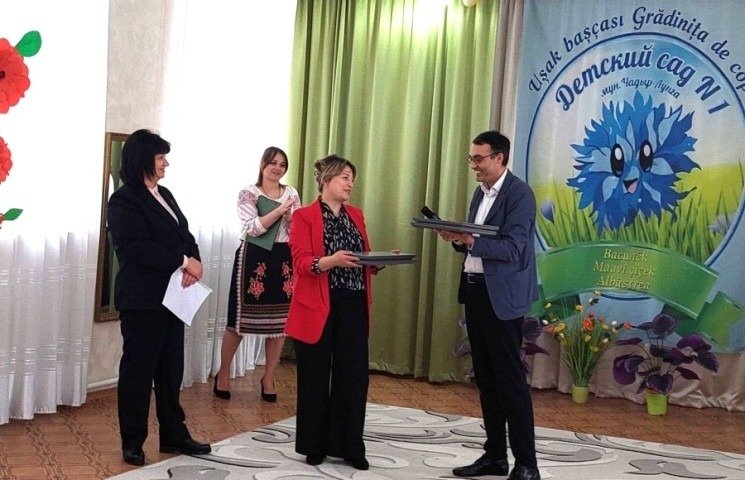 Три человека на сцене во время официальной церемонии передачи оборудования