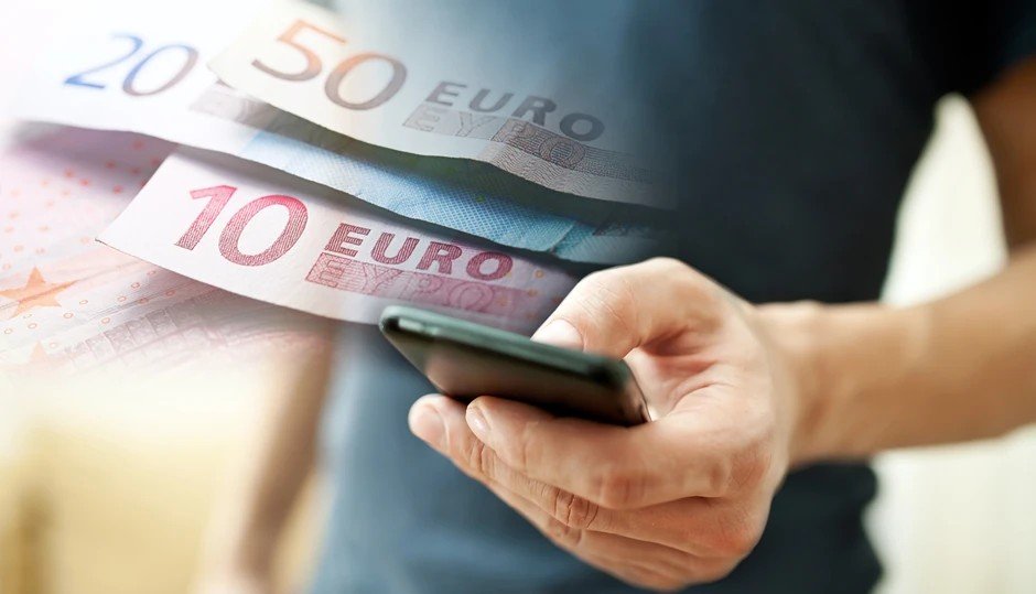 Мужчина пользуется смартфоном, держа купюры евро — мобильные переводы станут быстрее благодаря SEPA