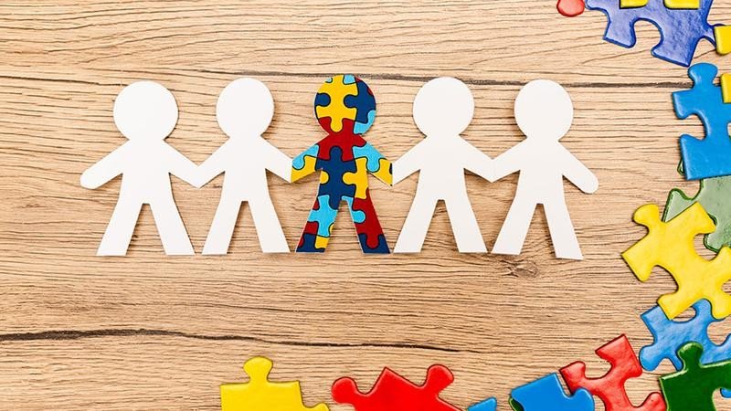 Символ инклюзии: бумажные фигурки людей, держащихся за руки, одна из которых украшена разноцветным пазлом — знаком осведомлённости об аутизме