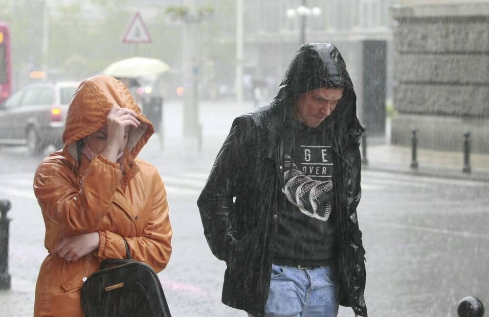 Двое прохожих пробираются по городской улице во время сильного ливня